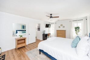 A modern bedroom with a large bed, wooden dresser, and a desk with a chair.