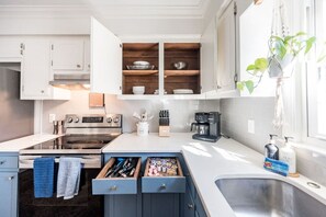 Una cocina moderna con armarios blancos, horno empotrado, cafetera y un lavamanos.