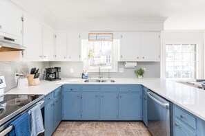 A modern kitchen with white cabinets, blue lower cabinets, a stainless steel sink, and a window with a view of the outdoors.