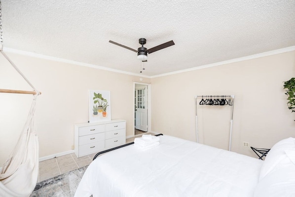 A bedroom with a bed, a wardrobe, a ceiling fan, a hanging plant, and a clothing rack.