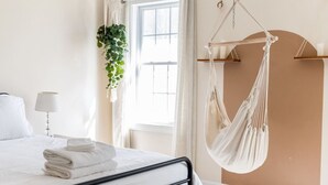 Un dormitorio con cama, una planta colgante, una hamaca y una ventana con cortinas.