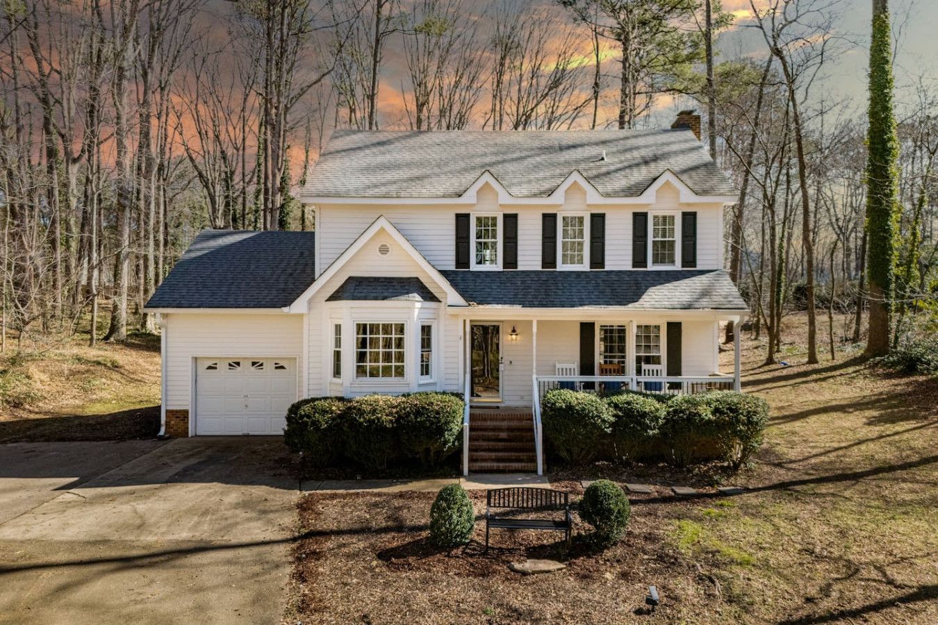 A two-story white house with a dark roof, a front porch, and a garage.