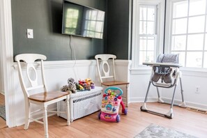 A room with two white chairs, a wicker basket with toys, a pink toy car, and a high chair.
