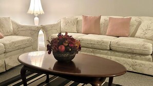 Un salon avec un canapé à motifs floraux, une table basse ronde en bois et un vase décoratif rempli de fruits et de fleurs.