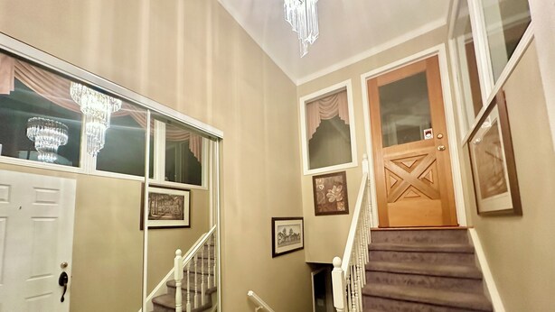 Un couloir avec une porte en bois, un escalier doté d’une rampe et un lustre.