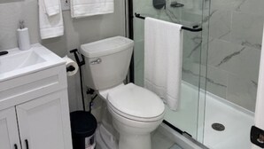 Ein modernes Badezimmer mit einer Glaskabine zur Dusche, weißen Armaturen und einer Duschwand aus Marmorplatten.