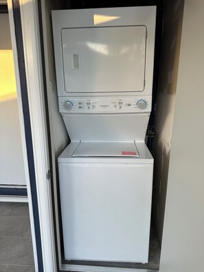 Une machine à laver blanche et compacte, dotée d’un panneau de commande, installée dans un espace étroit avec une porte sur un côté.