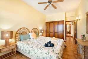 Quarto com cama, cabeceira de madeira, luminárias de cabeceira, ventoinha de teto, guarda-roupa, mesa de cabeceira e cômoda.