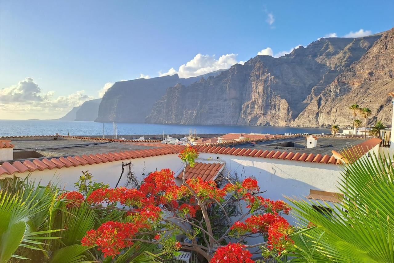 A coastal hotel with terracotta roofs, a view of the sea, and red flowers in the foreground.