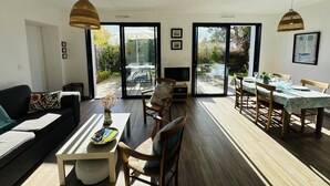 En rummelig opholdsstue med sofa, spisebord, stole, store vinduer og et fjernsyn.