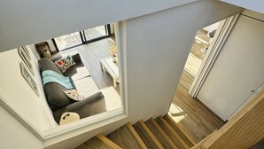 Et moderne interiør med en trætrap, en sofa med puder, og udsigt til opholdsstuen gennem et vindue.