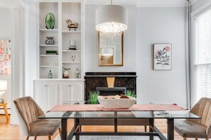 Un espace repas comprenant une table en verre, des chaises rembourrées, une cheminée et un lustre.