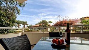 Une table à l’extérieur, avec une bouteille, un verre et une assiette d’oranges.