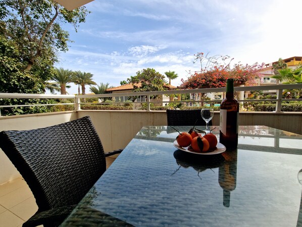 An outdoor table with a bottle, a glass, and a plate of oranges.