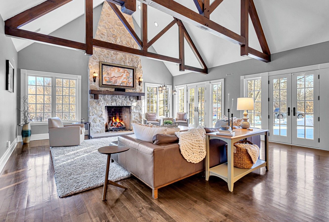 A spacious living room with a fireplace, wooden beams, and large windows.