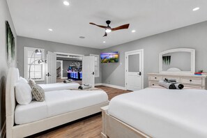 A bedroom with two beds, a TV, a ceiling fan, and a bar area in the background.