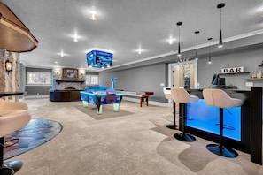 A modern bar area with a pool table, bar stools, and overhead lighting.