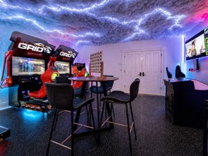 A gaming room with two racing simulators, a round table, and four chairs.
