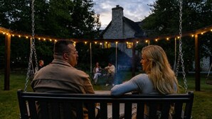 Una pareja sentada en un columpio en un jardín con un pabellón al fondo.