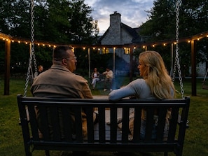 A couple sitting on a swing in a garden with a gazebo in the background.