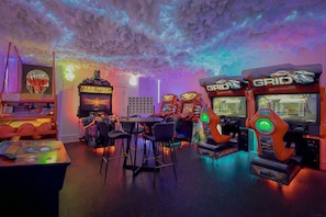 A gaming arcade with multiple arcade machines, a table with chairs, and a neon sign. - Baronwood Oasis | Pool + Arcade Mega Estate (Sheboygan)
