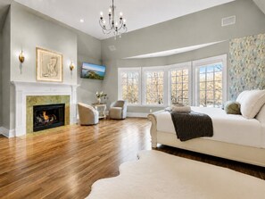 A spacious living room with hardwood flooring, a fireplace, a large window with multiple panes, and a white sofa. - Baronwood Oasis | Pool + Arcade Mega Estate (Sheboygan)
