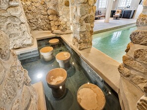 Zona de piscina con paredes de piedra y varios taburetes.
