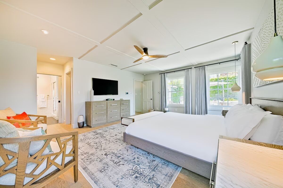 Une chambre d’hôtel moderne dotée d’un grand lit, d’un téléviseur à écran plat, d’un ventilateur de plafond et offrant une vue sur l’extérieur grâce à de grandes fenêtres.