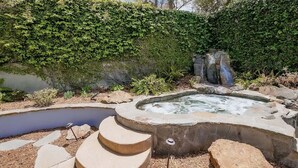 Un bain à remous entouré de rochers et un petit étang, avec des marches menant à celui-ci.