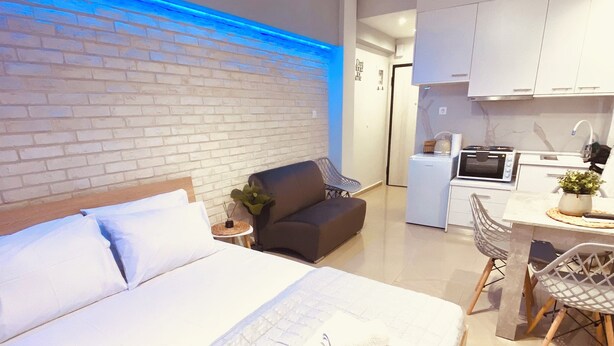 Une chambre d’hôtel moderne dotée d’un grand lit, d’une petite kitchenette, d’un coin salon avec un canapé et des fauteuils, et d’un mur décoratif en briques.