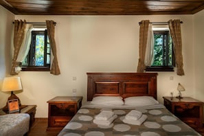 Une chambre à coucher avec une tête de lit en bois, deux tables de chevet, un lit recouvert d’une couvre-lit à motifs et des rideaux aux deux fenêtres.