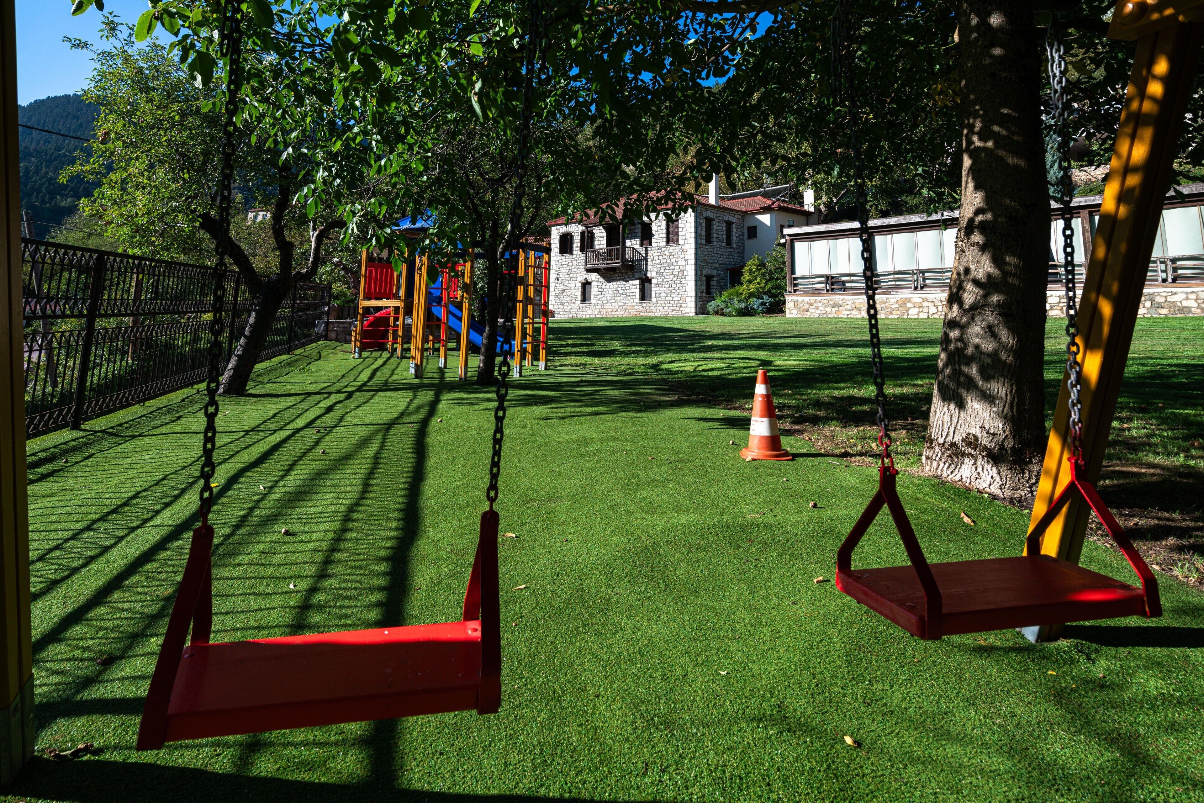 A playground with swings and climbing structures, surrounded by a fenced area and trees.