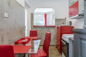 A compact kitchen with a dining area, red chairs, a glass table, and a red-framed window.
