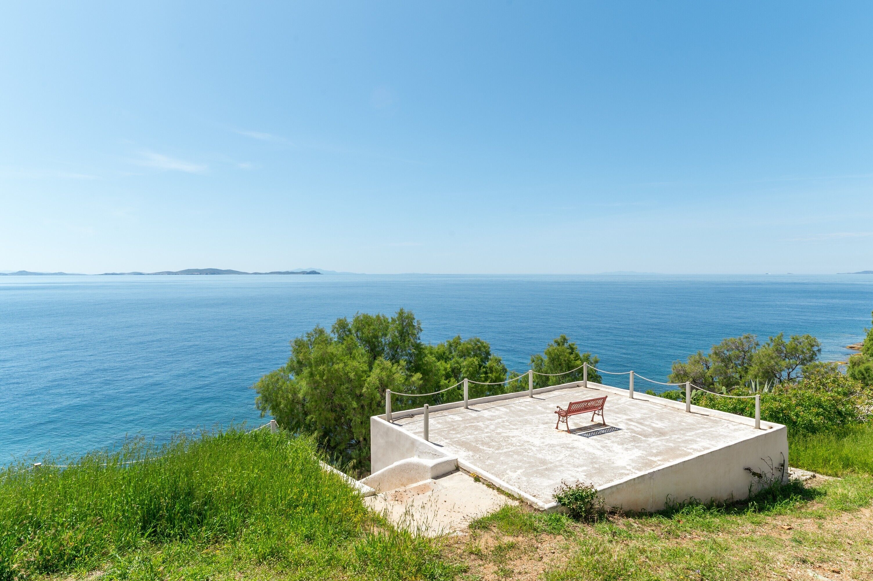 A concrete viewing platform with a bench, overlooking a body of water and distant land.