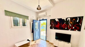 Una sala moderna con una mesa redonda de madera, un televisor de pantalla plana, un banco y una puerta que da a un balcón.