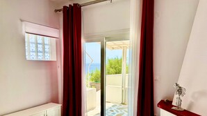 Una habitación con puerta corredera de vidrio que da a un espacio exterior, un radiador, una pequeña mesa con un adorno y una ventana con persianas.