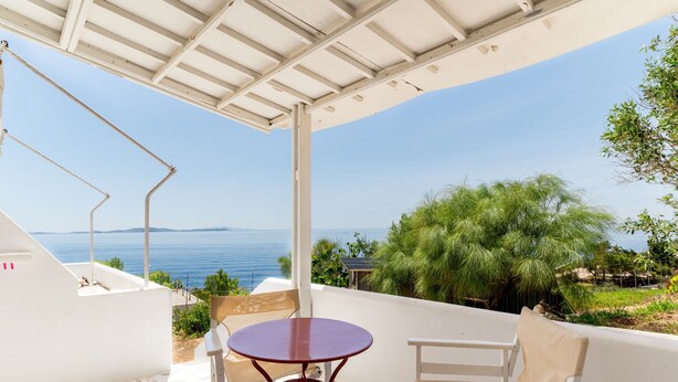 Un espacio de estar al aire libre con techo, con una mesa y sillas, que ofrece vistas panorámicas del mar y la vegetación.