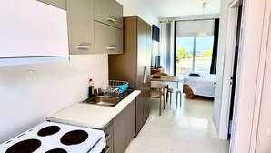 A modern kitchen with a stove, sink, and cabinets, leading to a dining area with a table and chairs. - Apartment 'Lefkopetra' with Shared Terrace, Wi-Fi and Air Conditioning (Tinos)