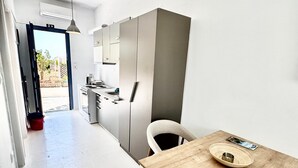 A modern kitchen with a wooden table and a chair, a red bucket, and a view of the outside. - Apartment 'Lefkopetra' with Shared Terrace, Wi-Fi and Air Conditioning (Tinos)