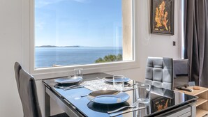 A dining table set with plates, glasses, and cutlery, a chair, a television, and a framed artwork on the wall. - Studio 'Theasea' with Private Garden, Wi-Fi and Air Conditioning (Tinos)