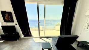A modern living room with a large sliding glass door leading to a balcony with a view of the sea. - Studio 'Theasea' with Private Garden, Wi-Fi and Air Conditioning (Tinos)