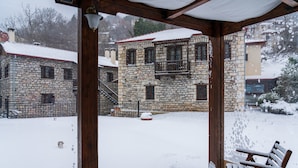 A stone building with a balcony, a wooden bench, and a snow-covered ground. - Double - Morea Room with Mountain View, Private Terrace, and Wi-Fi (Karpenision)