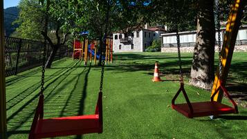 A playground with swings and climbing structures, surrounded by a fenced area and trees.