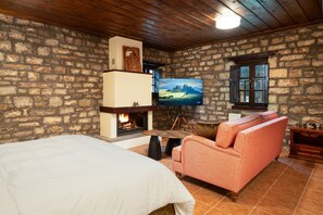 Une pièce avec un mur en pierre, une cheminée, une télévision, un canapé et un lit.