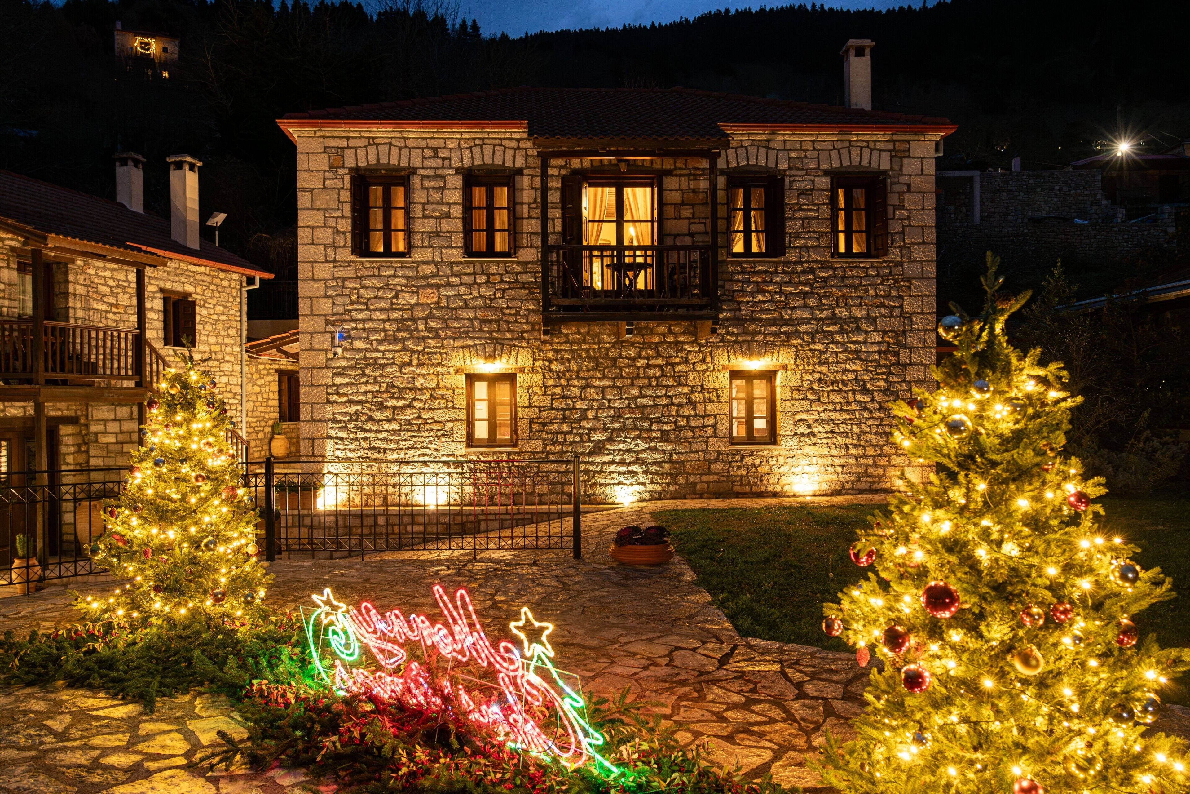 Un bâtiment en pierre doté de nombreuses fenêtres et d’un balcon, entouré d’un chemin en pierre et décoré pour Noël.