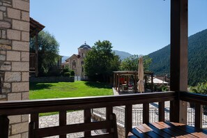 A stone building with a dome, a wooden deck with a table and chairs, and a view of a green lawn and mountains.
