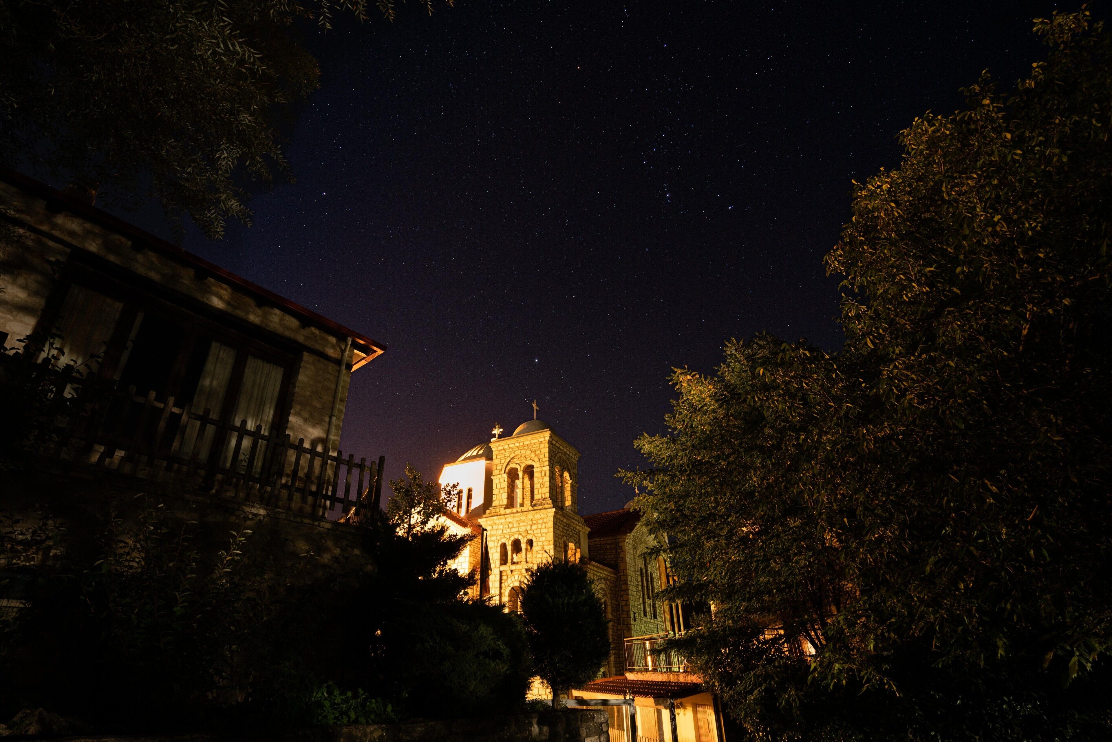 Une scène nocturne représentant une église illuminée par des lumières, entourée d’arbres et de bâtiments.
