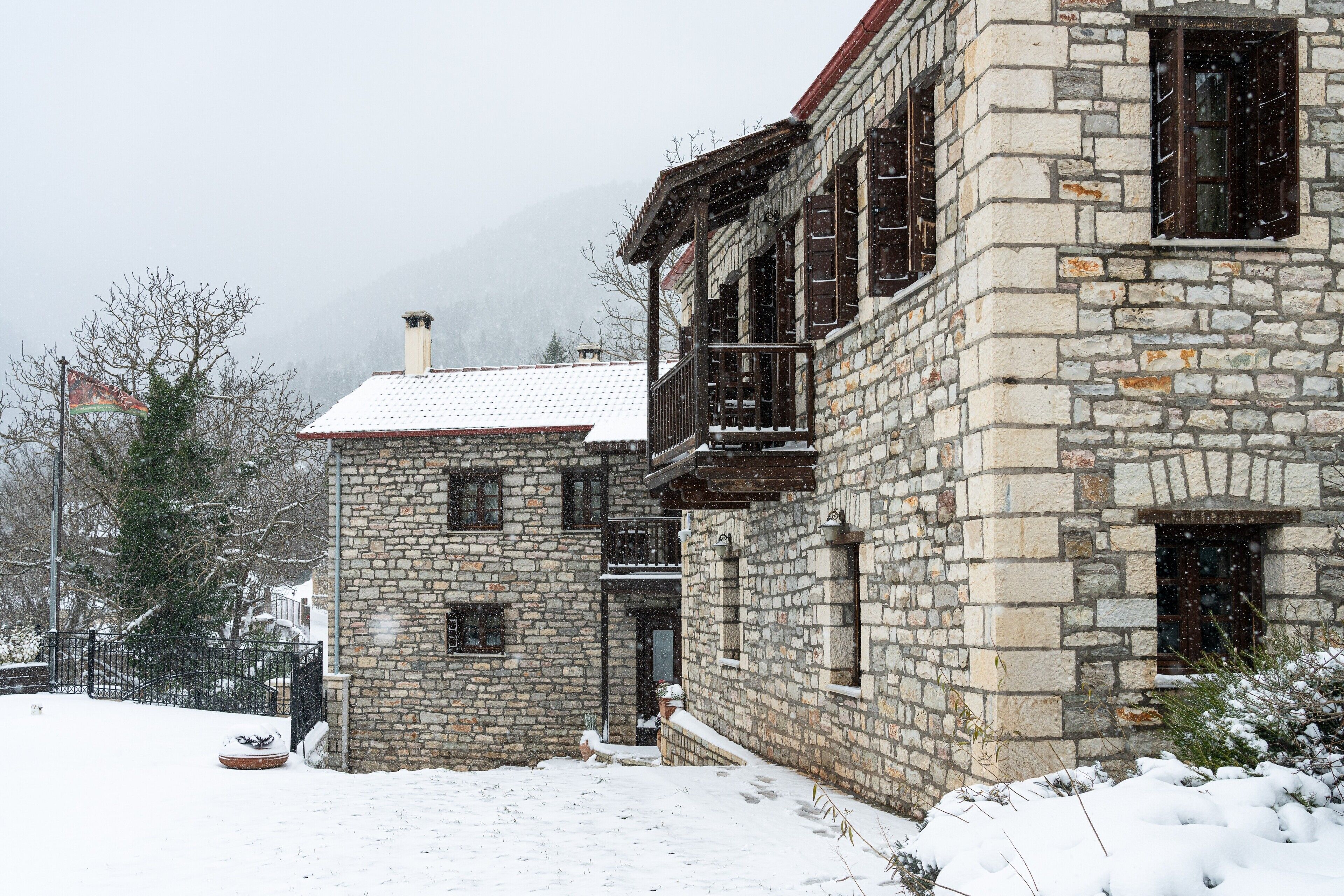 A stone building with a balcony, a snow-covered roof, and a visible chimney.