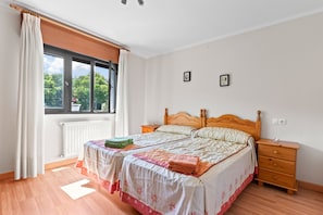 A bedroom with a bed, a nightstand, a window with curtains, and a radiator.