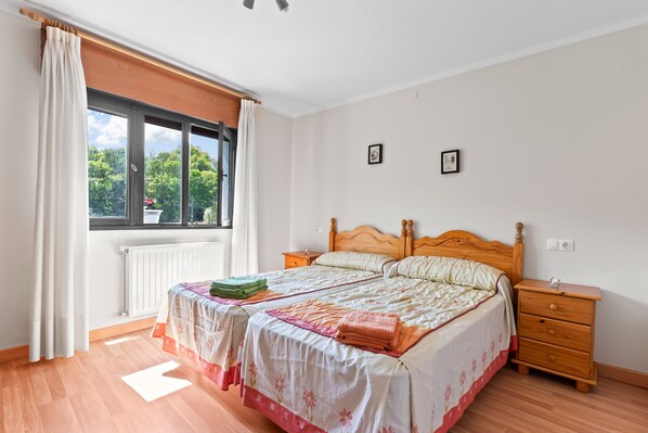 A bedroom with a bed, a nightstand, a window with curtains, and a radiator.
